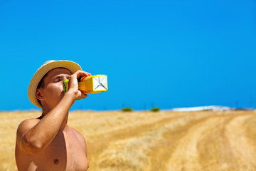 young guy with hat drinks juice on the field in summer