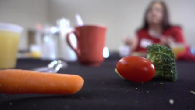 Slow Motion Vegetables Falling On Dirty Table With Plastic Fork And Knife And Cup With Person Eating In Background