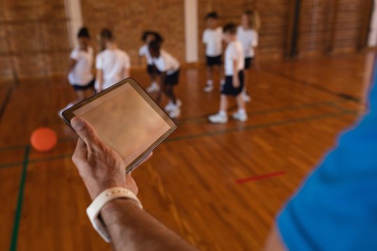 Basketball coach using digital tablet at basketball court in