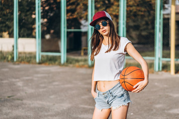 Pretty young sporty girl with basketball ball outdoor.