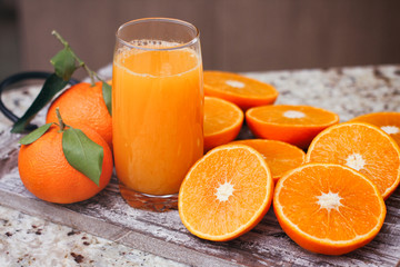 Glass with fresh citrus juice. Halves of tangerines and full fruits with leaves. Wood food stand.