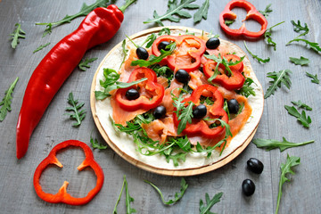 Tortilla posmarowana sosem chrzanowym, przykryta wędzonym łososiem, rukolą, papryką, i czarnymi oliwkami