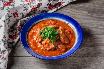 veal meat in tomato sauce with onion, garlic, chili peper on the wooden background. boiled meat and fresh tomato horizontal view