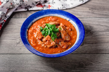 veal meat in tomato sauce with onion, garlic, chili peper on the wooden background. boiled meat and fresh tomato horizontal view