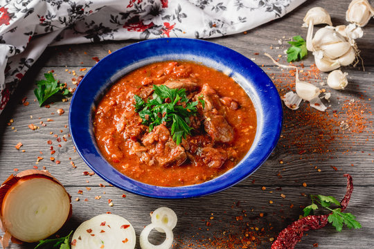Stewed veal meat with spices in a tomato sauce, veal meat in tomato sauce with onion, garlic, chili peper on the wooden background. boiled meat and fresh tomato horizontal view