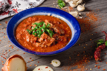 Stewed veal meat with spices in a tomato sauce, veal meat in tomato sauce with onion, garlic, chili peper on the wooden background. boiled meat and fresh tomato horizontal view