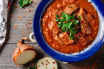 Stewed veal meat with spices in a tomato sauce, veal meat in tomato sauce with onion, garlic, chili peper on the wooden background. boiled meat and fresh tomato top view