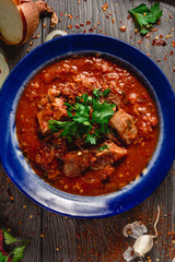 Stewed veal meat with spices in a tomato sauce, veal meat in tomato sauce with onion, garlic, chili peper on the wooden background. boiled meat and fresh tomato top view