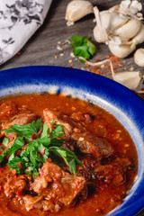 Veal meat with spices in a tomato sauce, veal meat in tomato sauce with onion, garlic, chili peper on the wooden background. boiled meat and fresh tomato top view