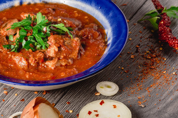 Stewed veal meat with spices in a tomato sauce, veal meat in tomato sauce with onion, garlic, chili peper on the wooden background. boiled meat and fresh tomato horizontal view