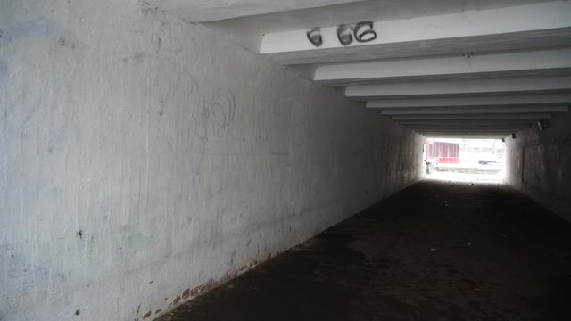 Man walking through the dark pedestrian underground crossing tunnel with light at the end and number of the beast 666 on the wall