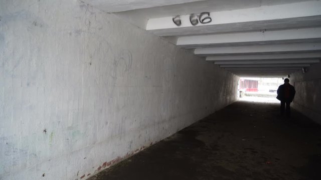 Man walking through the dark pedestrian underground crossing tunnel with light at the end and number of the beast 666 on the wall