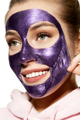 Close-up studio portrait of gorgeous young woman removing face mask and smiling. Good-looking model having spa day. Skincare beauty and cleansing concept