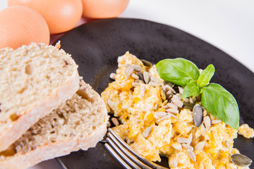 Scrambled eggs with sunflower and pumpkin seeds, some fresh eggs and wholemeal bread, eaten with a fork, decorated with basil, on a white background