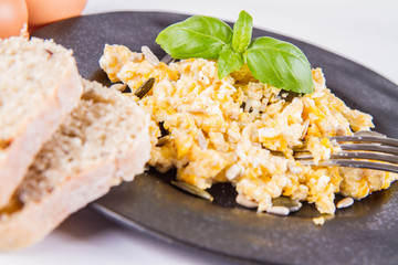 Scrambled eggs with sunflower and pumpkin seeds, some fresh eggs and wholemeal bread, eaten with a fork, decorated with basil, on a white background