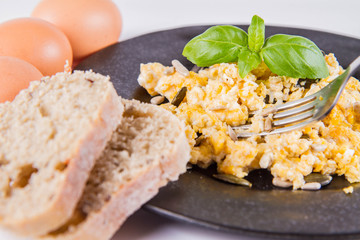 Scrambled eggs with sunflower and pumpkin seeds, some fresh eggs and wholemeal bread, eaten with a fork, decorated with basil, on a white background