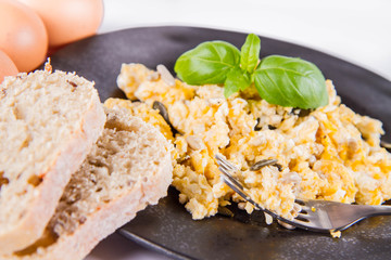 Scrambled eggs with sunflower and pumpkin seeds, some fresh eggs and wholemeal bread, eaten with a fork, decorated with basil, on a white background