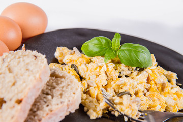 Scrambled eggs with sunflower and pumpkin seeds, some fresh eggs and wholemeal bread, eaten with a fork, decorated with basil, on a white background