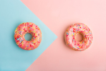 Two donuts decorated with sprinkles on colorful background. Coral and blue color background. Flat lay. Top view