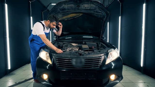 A Black Car Is Getting Fixed By A Man In Workwear