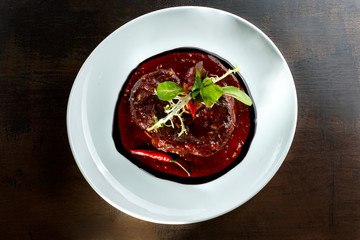 Meat with hot pepper sauce laid out on a white plate.