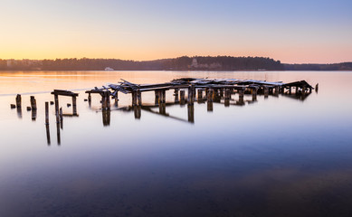 Fototapeta premium Destroyed bridge on the lake during a beautiful winter sunset