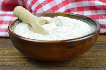 Whole wheat flour in wooden bowl, wooden background