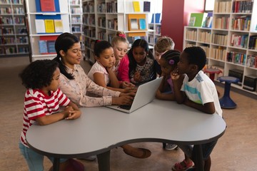 Female teacher teaching schoolkids on laptop at table in school