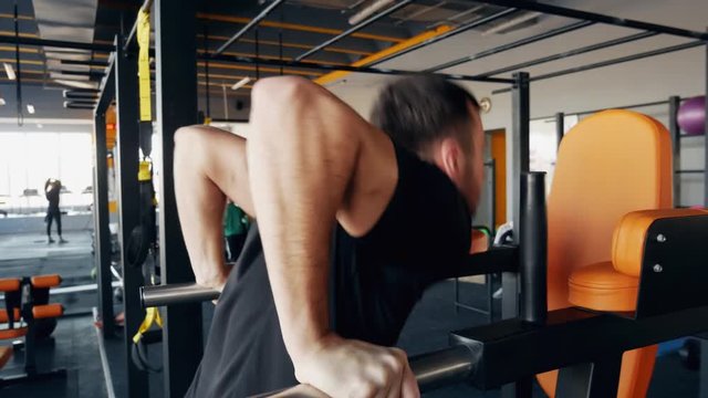 Muscular strong man push ups in gym on parallel bars in close-up