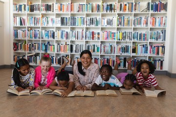 Female teacher and schoolkids reading a book while lying on