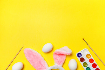 Happy Easter concept. Preparation for holiday. Decorative eggs colorful paints and bunny ears furry costume toy isolated on trendy yellow background. Simple minimalism flat lay top view copy space