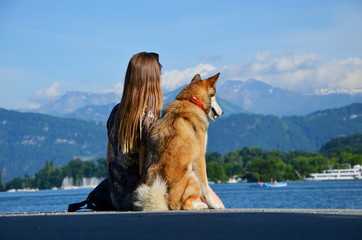Girl with dog sitting on pier and looking at mountains