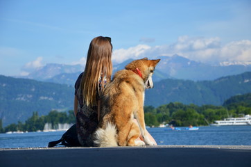 Girl with dog sitting on pier and looking at mountains