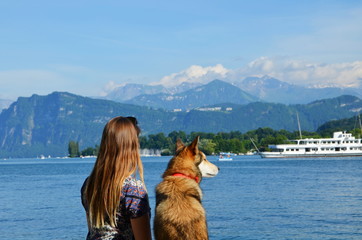 Girl with dog sitting on pier and looking at mountains