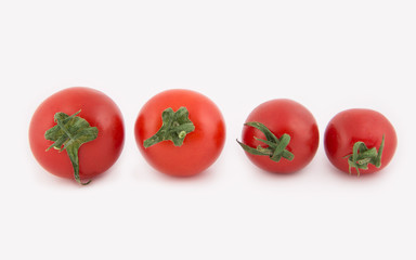 Four fresh cherry tomatoes lie in a row from the largest to the smaller. Tomatoes isolated on white background. Close-up photo