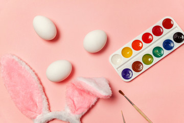 Happy Easter concept. Preparation for holiday. Decorative eggs colorful paints and bunny ears furry costume isolated on trendy pastel pink background. Simple minimalism flat lay top view copy space