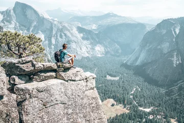 Washable wall murals Half Dome Young man sitting on the very edge of the cliff admiring Yosemite National park half dome cliff