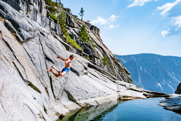 Young man jumping from the cliff into the  pond at Yosemite waterfall.