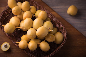 Fresh yellow dates on a sprig in wicker plate on rustic wooden background. Flat lay low key