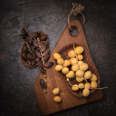 Fresh yellow dates on a sprig in wicker plate on wooden cuting board on dark background. Flat lay low key