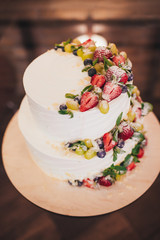 Three parts naked wedding cake with fruits and berries.