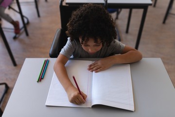 Schoolboy writing on notebook at desk in classroom