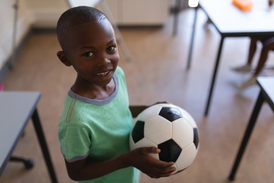 Smiling schoolboy holding football in classroom - Powered by Adobe