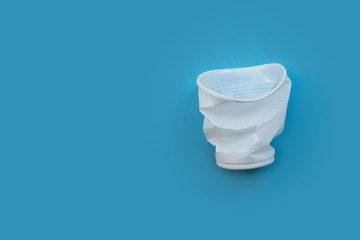 Crumpled white plastic cup on a blue background as a symbol of environmental pollution.