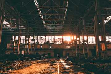 Abandoned ruined factory with columns and sunset light from broken glass windows, post apocalyptic...