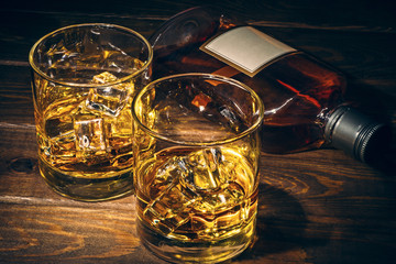 Two glasses of alcohol and bottle on dark wooden table