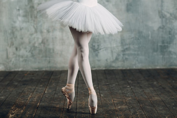 Ballerina in ballroom. Young beautiful woman ballet dancer, legs and pointe shoes and white tutu.