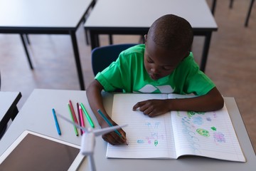 Schoolboy drawing on book at desk in classroom