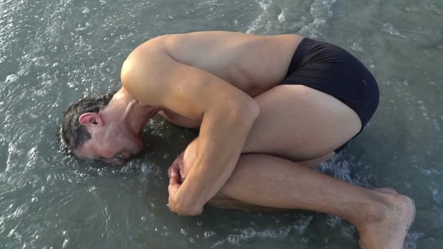 Man laying on the beach near the water in embryo pose. Evolution concept. Birth. Origin from the ocean