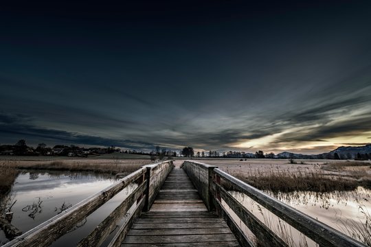 Holzsteg over the Ach with reflection and dramatic sky, Uffing, Staffelsee, Oberbayern, Germany, Europe
